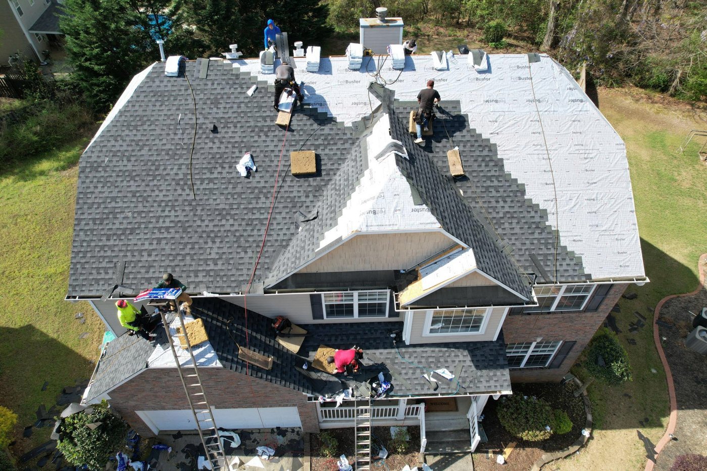 Roofing crew installing shingles beside exposed underlayment on a two-story home, Upstate SC