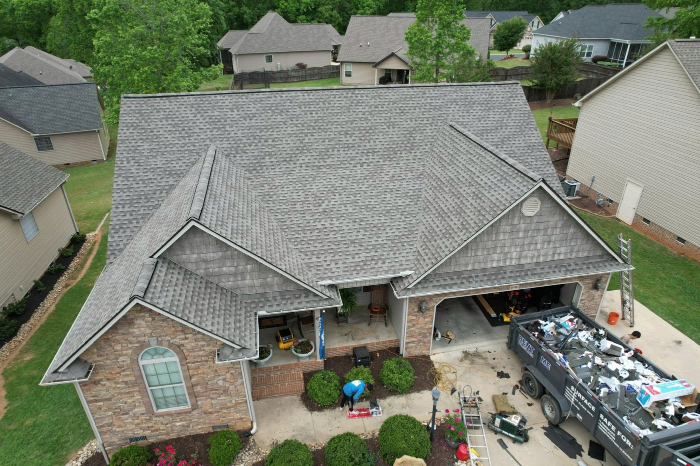 Drone view of a brick-and-stone home with a dump trailer in the driveway, Upstate SC