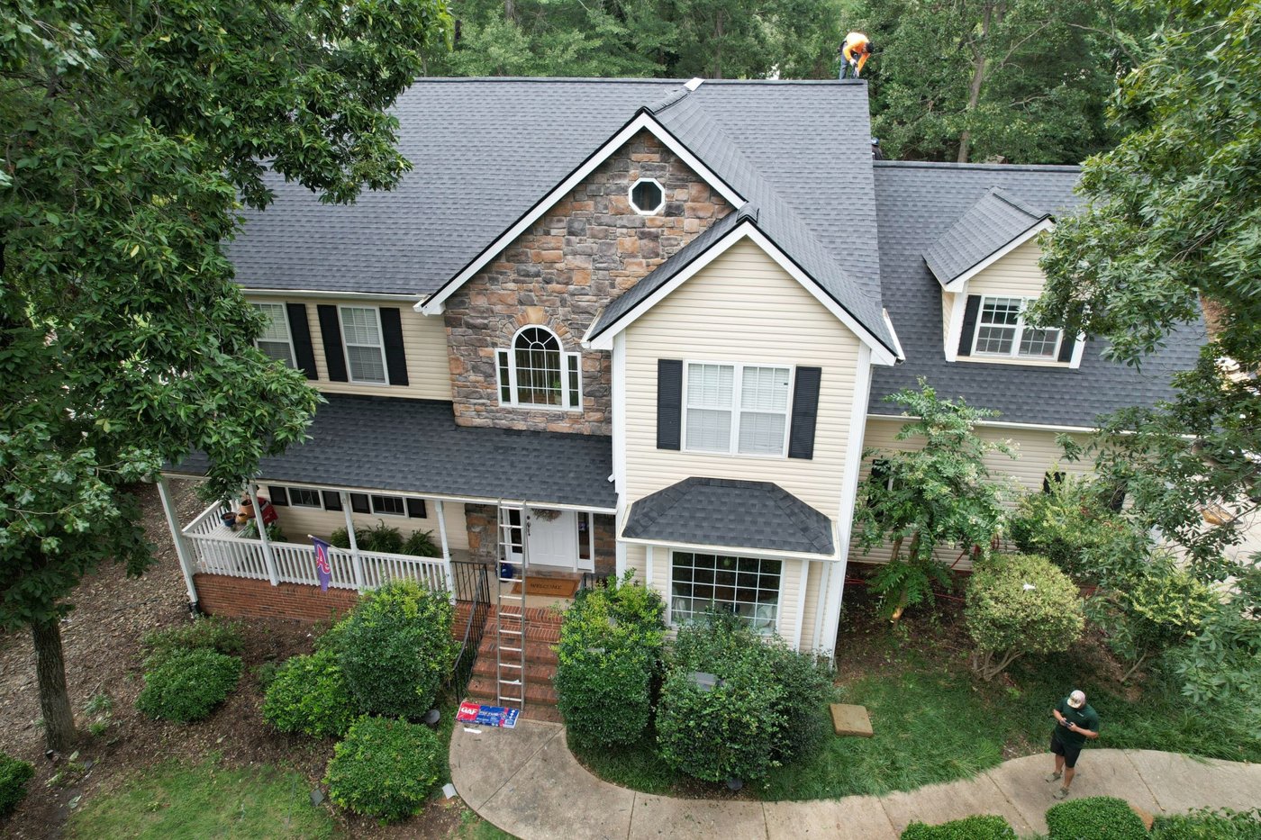 Drone view of a two-story stone-front home with a shingle roof, Upstate SC